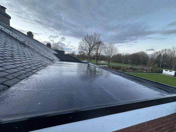 A flat roof covering finished with its black edge trim beside the slated slope